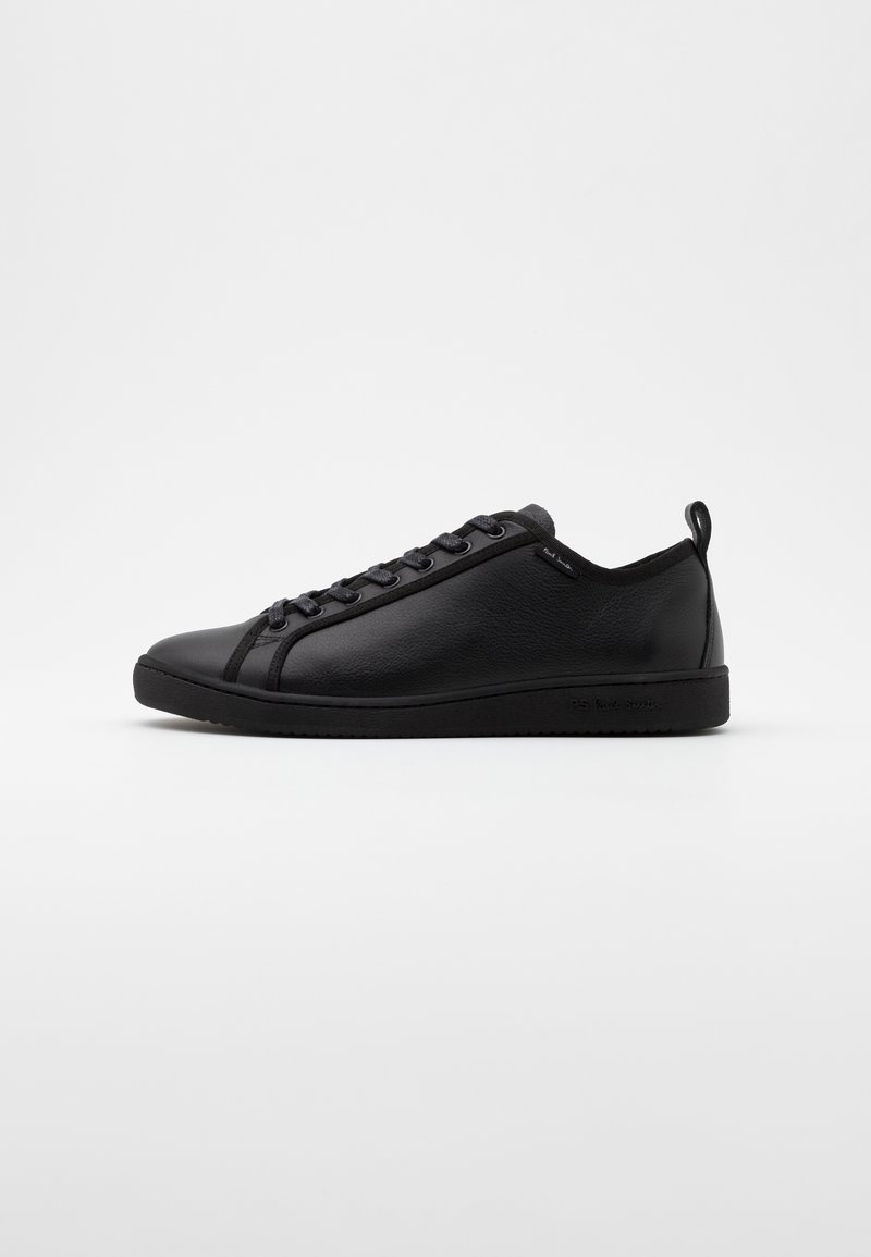 Baskets basses en cuir noir avec lacets noirs, bout arrondi et languette au talon sur fond gris clair.