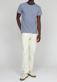 Gestreiftes Kurzarm-T-Shirt in Marineblau und Weiß, mit blauem Kragen, kombiniert mit cremefarbenen Hosen und beigen Sneakern.