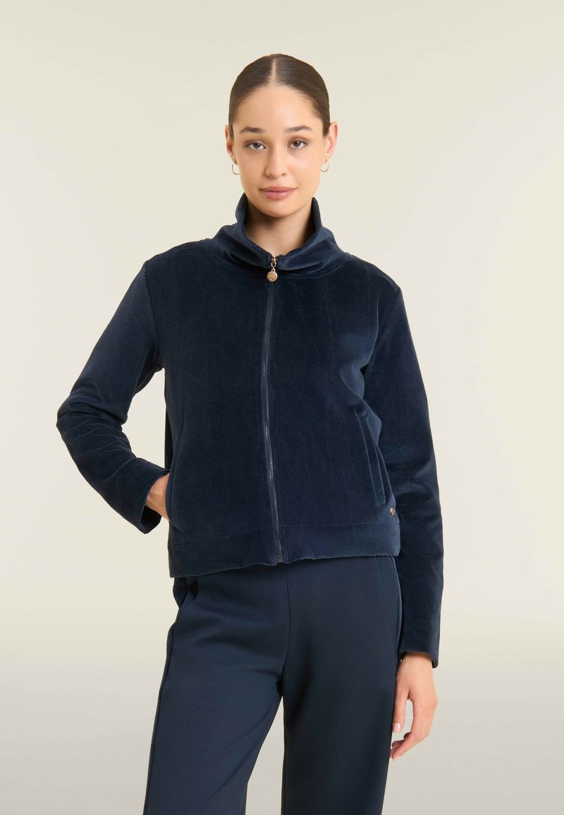 Giacca zip-up in corduroy blu navy con colletto alto, dettagli delle cuciture in evidenza e tasca frontale, dotata di una zip arrotondata.
