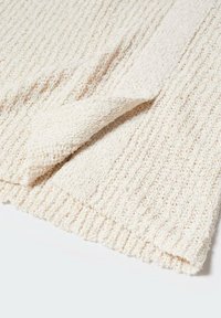 Tessuto a maglia di colore crema con texture, presenta un angolo ripiegato che mostra il motivo a costine e dettagli in filato morbido e ad ansa.