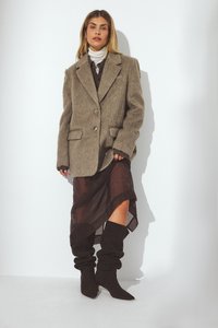 Chlpaté béžové oversize sako s dvoma gombíkmi a bočnými vreckami, prekryté priehľadnou tmavou sukňou a čiernymi vysokými čižmami.