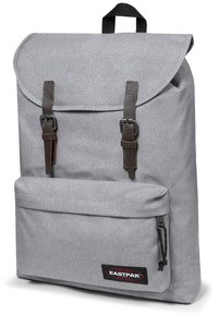 Zaino in tessuto grigio con chiusura a rotolo, spallacci in pelle marrone, tasca frontale e patch del logo Eastpak nella parte inferiore.
