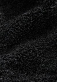 Zwarte stof met een gestructureerd, pluche oppervlak, met een zachte, donzige textuur. Het materiaal lijkt dik en knus met een egale kleur.