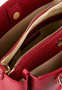 Intérieur de sac à main en cuir rouge texturé avec une fermeture éclair dorée, une doublure crème et des détails en métal. Compartiments et poches visibles.