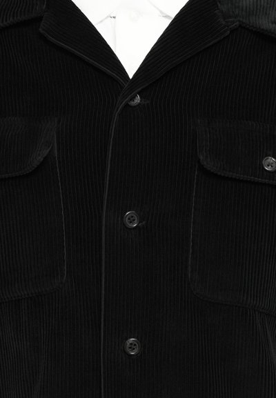 Black corduroy jacket featuring a notched collar, two chest pockets, and four buttons. Textured vertical ridges throughout the fabric.