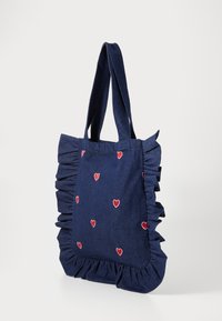 Denim iepirkumu soma ar viļņotām malām, tumši zila krāsa, rotāta ar maziem sarkaniem sirsniņu izšuvumiem visā virsmā, izturīgas rokturiem ērtai nēsāšanai.