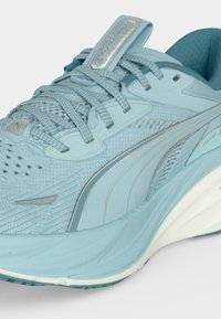 Αθλητικό παπούτσι ανοιχτού μπλε χρώματος με άνω μέρος από δίχτυ, συνθετικές επιφάνειες, κορδόνια, μαλακή σόλα και λογότυπο Puma στη γλώσσα και στην πλευρά.