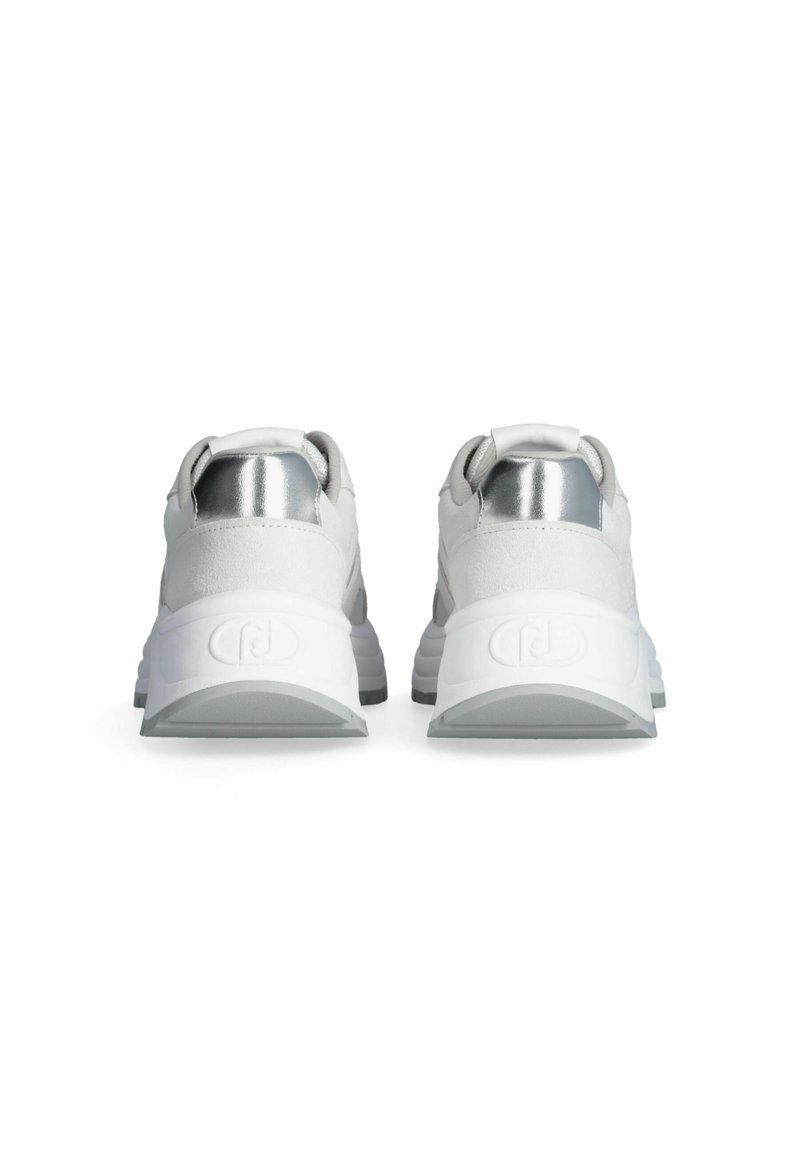 Zapatillas blancas con parte superior texturizada, que presentan detalles plateados en el talón y una suela gruesa y acolchada en gris para mayor comodidad y soporte.