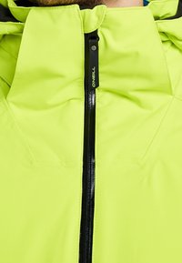 Fermeture éclair d'une veste jaune-vert vif partiellement fermée avec une languette noire portant la mention "O'Neill", montrant une partie du cou et du menton d'une personne.