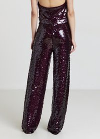 Combinaison pailletée en bordeaux profond, avec un corsage ajusté et un pantalon évasé. Présente un design sans dos et une texture brillante grâce aux sequins.