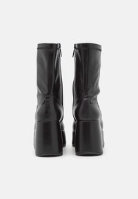 Bottines en cuir noir avec talons carrés, dotées d'une finition lisse, de coutures verticales et de fermetures éclair latérales pour un enfilage facile.