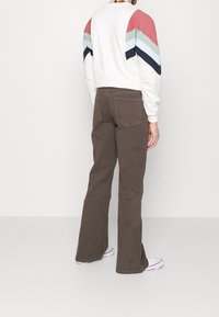 Ruskeat levenevät housut, joissa on viiden taskun malli, hienovarainen tekstuuri ja näkyvät saumat. Yhdistetty valkoiseen svetariin, jossa on moniväriset raidat.