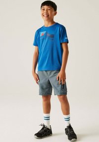 Camiseta deportiva corta de manga azul con gráfico de montaña, combinada con pantalones cortos grises, calcetines blancos con rayas azules y zapatillas deportivas negras.