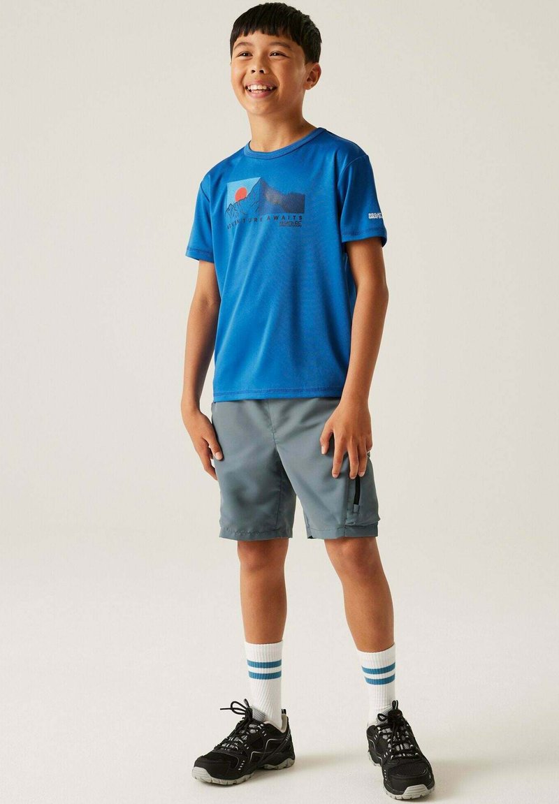 Camiseta deportiva corta de manga azul con gráfico de montaña, combinada con pantalones cortos grises, calcetines blancos con rayas azules y zapatillas deportivas negras.