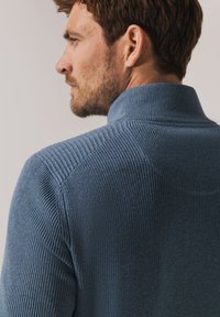 Blue ribbed knit sweater with a high collar and textured detailing on the shoulders. Material appears soft and fitted.