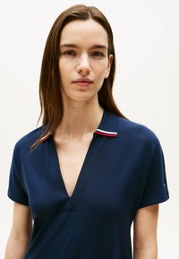 Camisa polo azul marino con escote en V, mangas cortas y cuello con acentos en rojo y blanco. Tejido texturizado con un diseño ajustado.