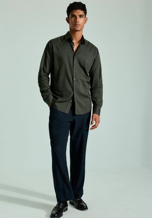 Dark green button-up shirt with a geometric pattern, paired with navy blue trousers and black shoes. Smooth fabric, tailored fit.
