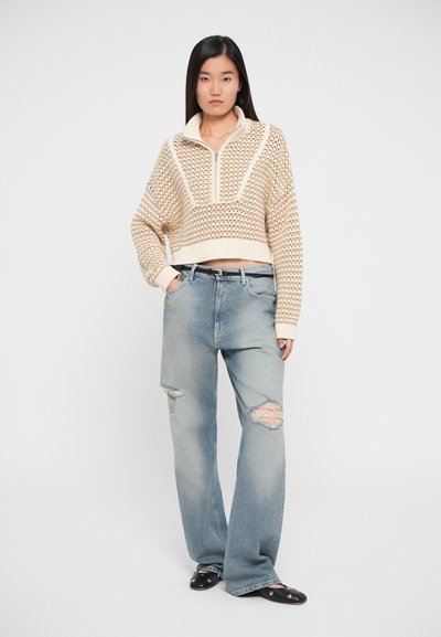 Knit cream pullover with a half-zip collar and textured diamond pattern, paired with light blue ripped wide-leg jeans and black mules.