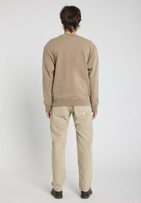 Sweat-shirt en coton brun avec col ras du cou, coupe oversize et poignets côtelés, associé à un pantalon beige et des chaussures sombres. Palette de couleurs neutres.