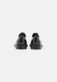 Schwarze Lacklederschuhe mit glatter Oberfläche, runder Zehenform und niedrigem Absatz. Mit einer Zuglasche an der Rückseite für ein einfaches Anziehen.