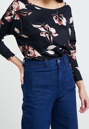 Top lungo a maniche con stampa floreale scura, dettagli in rosa e crema, abbinato a jeans in denim blu a vita alta, dotati di due tasche posteriori.
