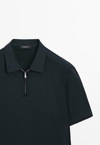 Czarna koszulka polo z krótkim rękawem, kołnierzykiem i srebrnym suwakiem z przodu, pokazana na białym tle.