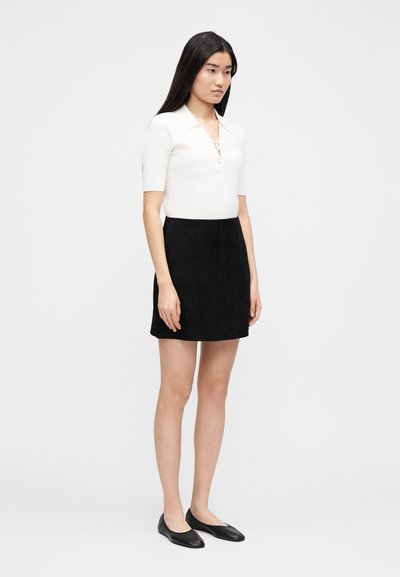 White ribbed short-sleeve polo shirt with a collar, paired with a black suede mini skirt and black flat shoes, slim fit silhouette.