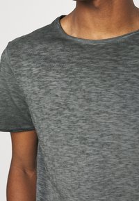 Camiseta gris de manga corta con una superficie lisa y ligeramente texturizada. Cuello redondo y corte clásico, con un sutil patrón jaspeado.