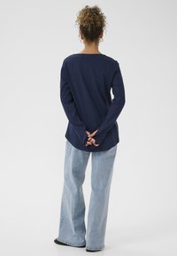 Maglietta a maniche lunghe blu navy con scollatura rotonda, abbinata a jeans a gamba larga blu chiaro. Il tessuto sembra morbido con dettagli di cucitura precisi.