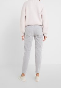 Pantalones de pana gris claro con un corte relajado y bolsillos traseros, combinados con un suave suéter de canalé rosa claro y zapatillas beige.