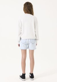 Camiseta de manga larga gris combinada con pantalones cortos de mezclilla azul claro. Zapatillas altas negras presentan un logo blanco. Diseño suave y casual.