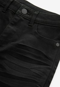 Sorte denimjeans med en glat tekstur, der har subtile falmninger og slidte detaljer. Metalknap og syninger i matchende farve.