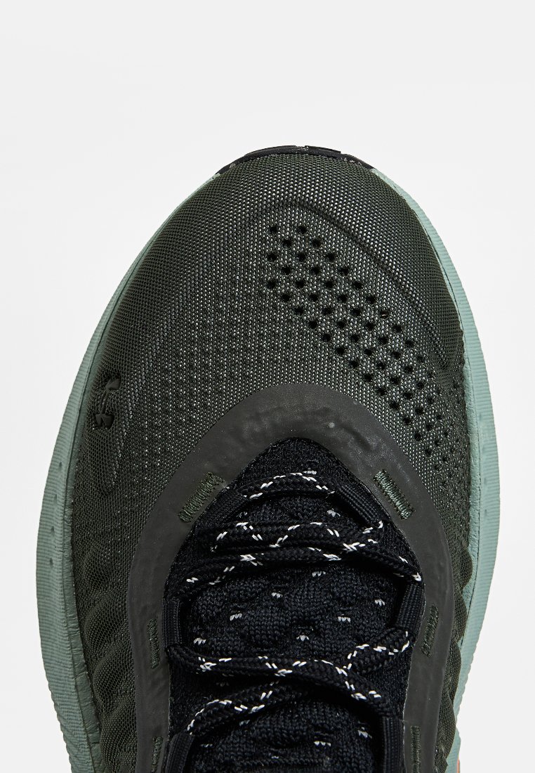 Chaussure de sport avec un dessus texturé gris foncé, lacets noirs et semelle vert menthe. Présente des perforations et un collier rembourré.
