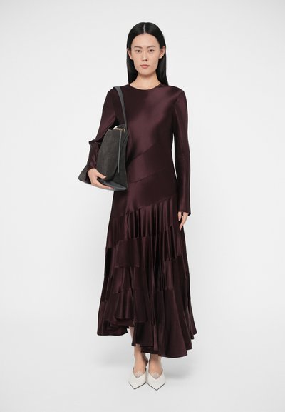 Garš bordo krāsas satīna svārks ar kārtojuma volāniem, garām piedurknēm, pieguļošu korseti un apaļu kakla izgriezumu; kopā ar tumšu plecu somu un baltām kurpēm.