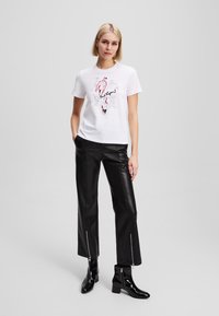 White t-shirt with graphic print and black lettering, paired with black leather pants featuring zippers at the ankles and black ankle boots.