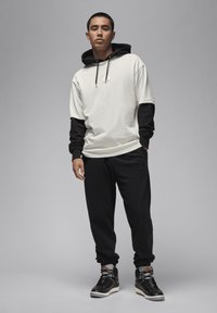 Felpa grigia chiara con maniche e cordini neri, abbinata a pantaloni jogger neri e sneaker alte nere. Design semplice e sportivo.