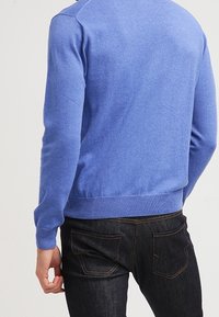Hellblauer Strickpullover mit gerippten Bündchen und Saum, Rundhalsausschnitt und glatter Textur, kombiniert mit dunklen Jeans mit Gesäßtaschen.