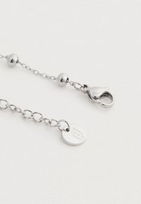 Strieborný náhrdelník s okrúhlymi perličkami, spona na homára a kruhová visačka s vygravírovaným logom na bielom pozadí.