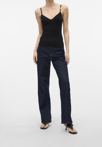 Czarny prążkowany top na ramiączkach z cienkimi paskami, w połączeniu z ciemnoniebieskimi prostymi dżinsami. Modelka ma na sobie czarne sandały na obcasie z paskami.