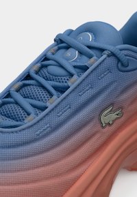 Baskets en dégradé bleu et rose avec une surface texturée en mesh et matériau synthétique, fermeture à lacets, et un petit logo crocodile.