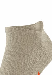 Calzino beige alla caviglia con texture a coste e tallone rinforzato. Presenta un piccolo logo rosso vicino alla punta. Tessuto morbido, polsino elastico.