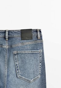 Vue arrière d'un jean en denim bleu clair avec une seule poche arrière et un patch de marque en cuir noir sur la ceinture.
