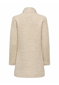Manteau beige texturé avec une apparence douce et légèrement duveteuse. Il présente un col et de longues manches, mettant en avant une silhouette simple et droite.