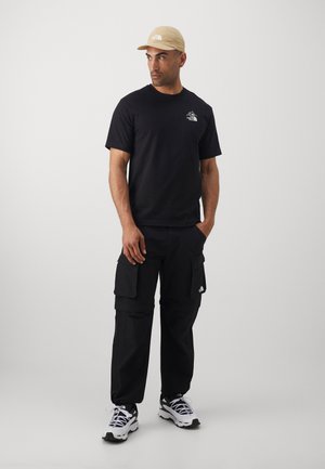 Black cotton T-shirt with logo, black cargo pants with pockets, beige cap, and white sneakers with black accents. Simple, functional design.