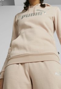Sweat à capuche rose pâle avec une poche kangourou, arborant un logo Puma argenté. Confectionné en tissu doux avec un ourlet et des poignets côtelés.