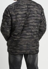 Grå og sort camouflagejakke med polstring og høj krave, med quiltet design og sidelommer. Bagsiden viser form og tekstur.