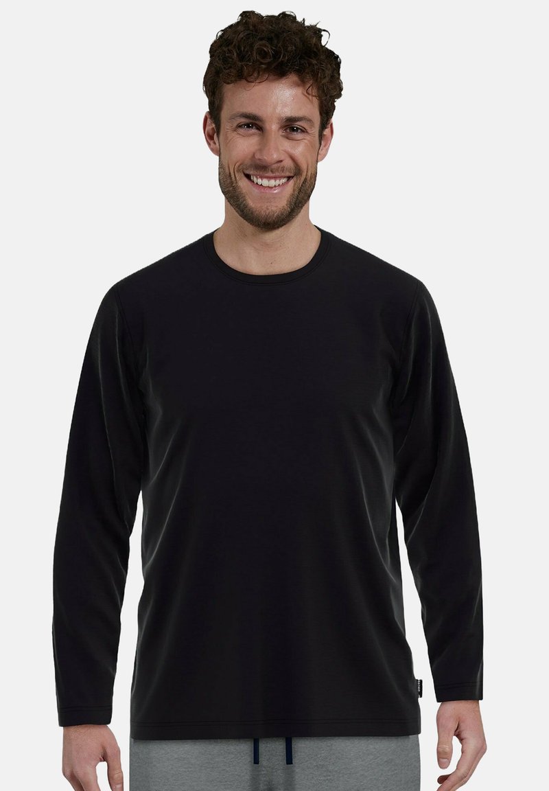 Camisa negra de manga larga con textura suave y cuello redondo, combinada con pantalones grises, con un ajuste casual y detalles de diseño minimalistas.