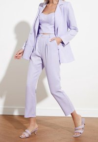 Licht lila op maat gemaakt pak met een blazer en hoge taillebroeken. Gladde stof, cropped top en sandalen met hoge hakken en bandjes.