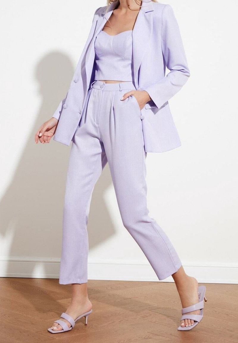 Licht lila op maat gemaakt pak met een blazer en hoge taillebroeken. Gladde stof, cropped top en sandalen met hoge hakken en bandjes.