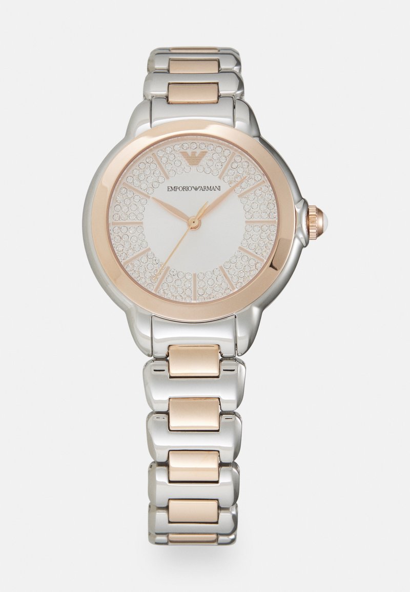 Silver- och rosaguldmetal klocka med en rund urtavla prydd med kristaller. Den har en vit urtavla med timmarkörer och en lysande krona.